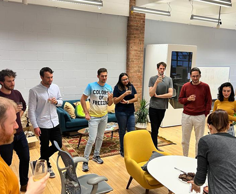 A group of people standing around a table waiting for birthday cake.
