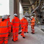 A group of people in high visibility clothing and hard hats at a cement plant.